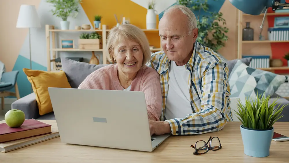 Elderly couple looking at a GENERIC NOT-A-MAC laptop in what looks like an IKEA sales floor setup. Seriously, I think if you zoom in you can see the price tags.